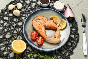 Plate of tasty salmon steak with tomatoes, garlic and lemon on grey background