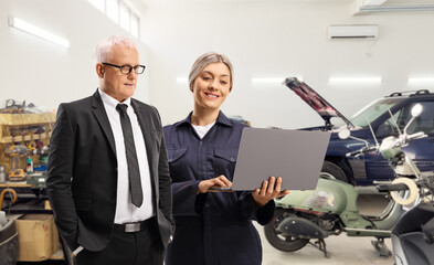 Female auto repair mechanic showing a laptop computer to a man