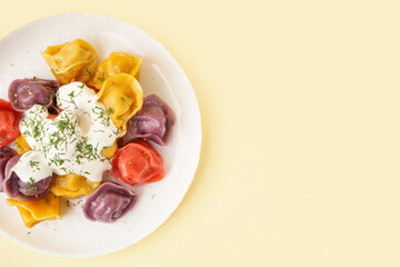 Plate of boiled colorful dumplings with sour cream and dill on yellow background