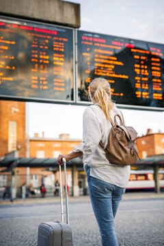 Solo travel on vacation. Woman passenger is checking arrival and departure board schedule timetable at bus station