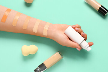 Female hand with bottles of makeup foundation, sponges and samples on turquoise background