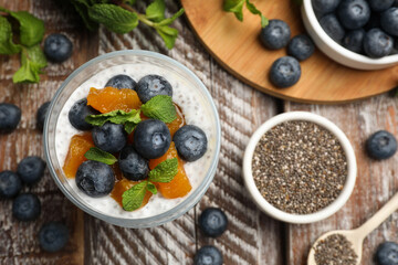 Delicious chia pudding with blueberries, peaches and mint in glass on wooden table, flat lay