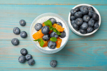 Delicious chia pudding with blueberries, peaches and mint in glass on light blue wooden table, flat lay