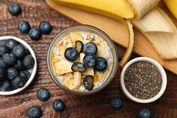 Delicious chia pudding with blueberries, banana and oatmeal in glass on wooden table, flat lay