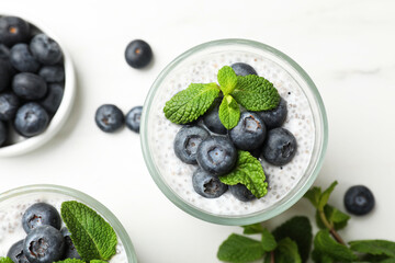 Delicious chia pudding with blueberries and mint in glasses on white table, flat lay