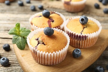 Delicious muffins with blueberries and mint on wooden table, closeup