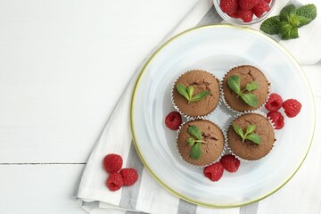 Delicious muffins with raspberries and mint on white wooden table, top view. Space for text