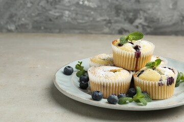 Delicious muffins with blueberries, powdered sugar and mint on grey textured table, closeup. Space for text