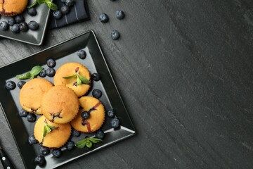 Delicious muffins with blueberries and mint on dark textured table, flat lay. Space for text