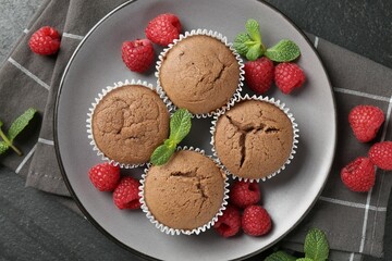 Delicious muffins with raspberries and mint on dark textured table, top view