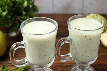 Healthy parsley drink in glasses, leaves and apples on wooden table, closeup