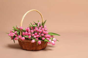 Bouquet of beautiful tulips in wicker basket on beige background, space for text