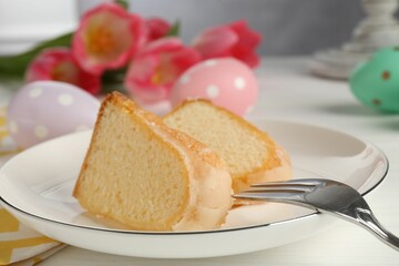 Pieces of delicious bundt cake, Easter eggs and tulips on white wooden table, closeup