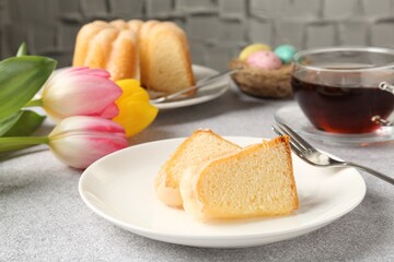 Pieces of delicious bundt cake, Easter eggs, tulips and tea on gray table, closeup