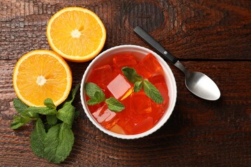Delicious jelly cubes in bowl, mint, orange and spoon on wooden table, flat lay