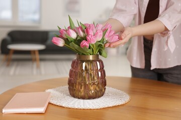 Woman with bouquet of pink tulips at wooden table indoors, closeup