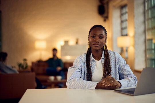 Confident Professional Woman Sitting in Modern Office Environment with Laptop