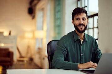Obraz premium Smiling Man Working on Laptop in Bright and Modern Office Environment