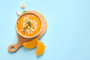 Bowl of delicious pumpkin cream soup with basil, seeds and garlic on blue background