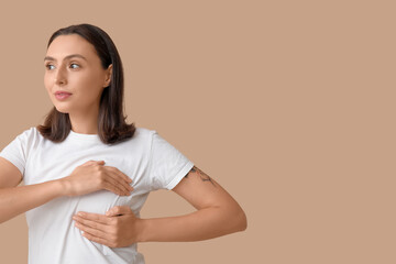 Fototapeta premium Young woman checking her breast on beige background. Cancer awareness concept