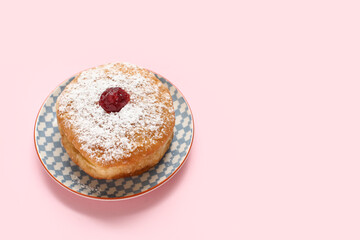 Plate with tasty donut for Hanukkah celebration on pink background