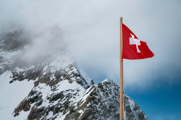 The Swiss flag fluttering in the snowy mountains of the Swiss Alps