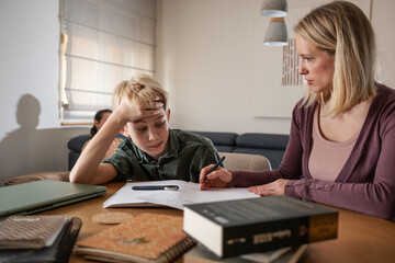 A mother, helping her son with his homework. They are using a laptop to search for information and...