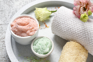 Tray with body scrubs, bath supplies and flowers on grunge background, closeup