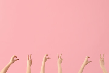 Female hands showing peace and heart gestures on pink background