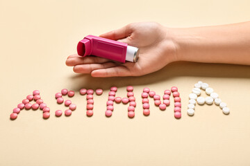 Child's hand with inhaler and word ASTHMA made of pills on beige background
