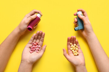 Child's hands with asthma inhalers and pills on yellow background