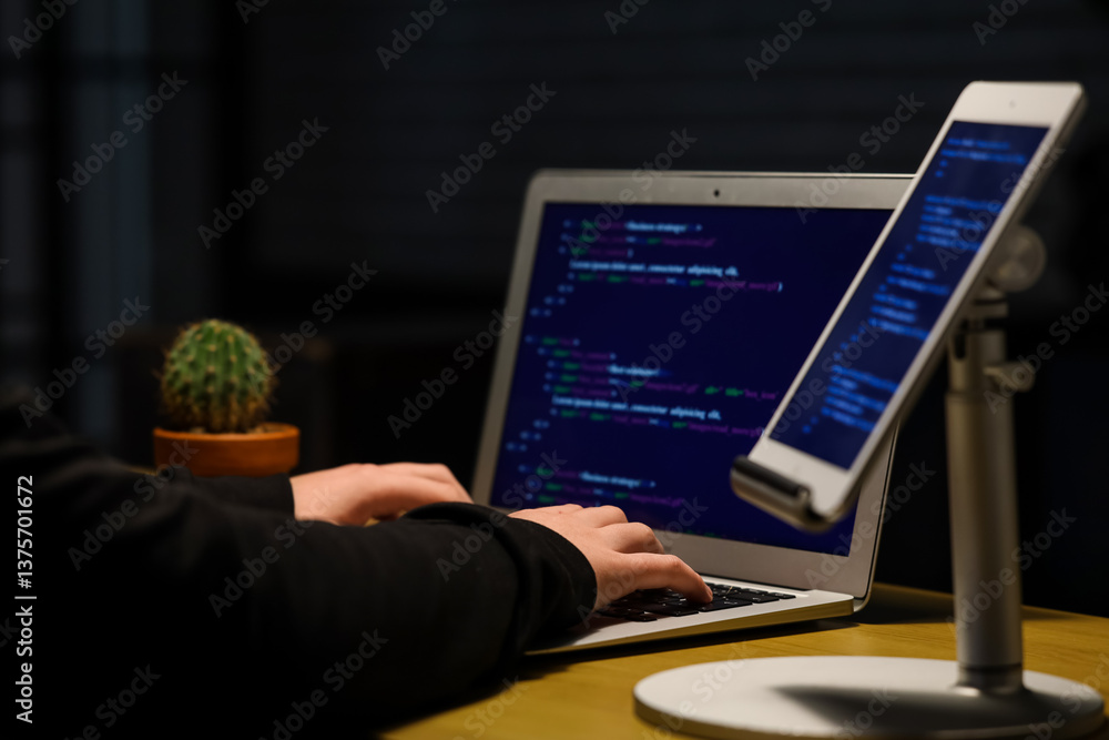 Poster hacker using laptop at table in dark room, closeup