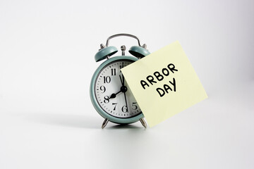 Alarm Clock With Arbor Day Reminder Note. alarm clock with handwritten "ARBOR DAY" sticky note, symbolizing tree planting celebration and environmental awareness reminder. Arbor day concept