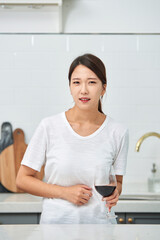 A young Asian woman at the kitchen table holding a wine glass, struggling with a hangover from the...