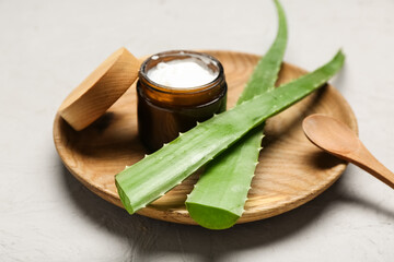 Wooden plate with jar of cosmetic product and aloe vera leaves on grey background