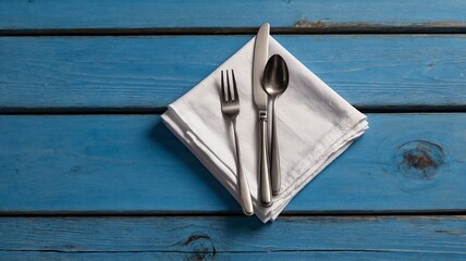 Elegant silverware placed on a white napkin atop a bright blue wooden table.