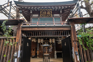 A weathered wooden shrine gate in Osaka, Japan. Lanterns hang, a statue stands, showing traditional Asian architecture and religious elements.