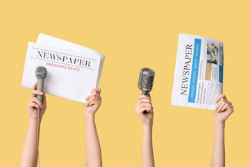 Female hands with newspapers and microphones on yellow background