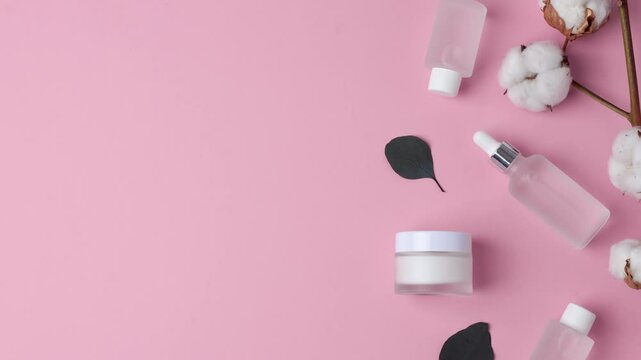 Cosmetic skin care products with flowers and eucalyptus on pink background. Flat lay, copy space