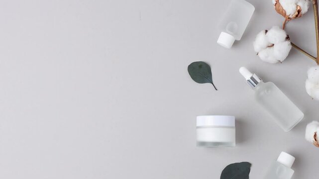 Cosmetic skin care products with flowers and eucalyptus on grey background. Flat lay, copy space