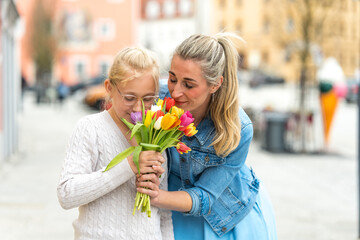 Fototapeta premium A young girl gives flowers to her smiling mother on Mother's Day