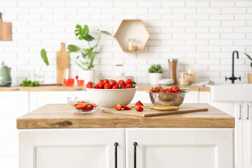 Bowl, colander and board with tasty strawberries on table in kitchen