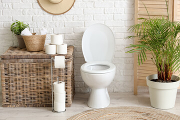 Toilet bowl, laundry basket and folding screen near white brick wall in restroom