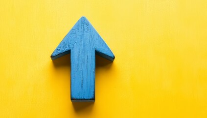 On a yellow backdrop, a blue wooden arrow points upwards, representing business and market expansion. Flat lay