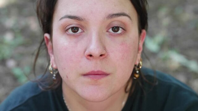 Vertical: Young brunette woman looks dejectedly at the camera, her expression reflecting sadness and unhappiness.