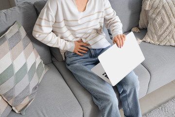 Young woman with laptop suffering from severe abdominal pain at home, closeup