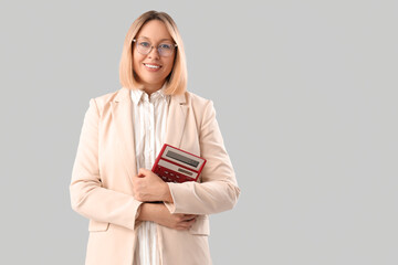 Mature female math teacher with calculator on grey background