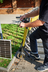 Man connects solar panel to electric scooter for charge, highlighting practical application of...