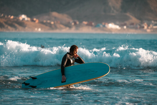 Surfer carrying a surfboard on a beach, summer sunset surf scene