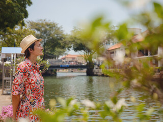 Fototapeta premium Young woman in ethnic dress and hat exploring the vibrant streets of Malacca, Malaysia. A blend of cultural heritage, colorful architecture, and tropical charm. Perfect travel and lifestyle moments.